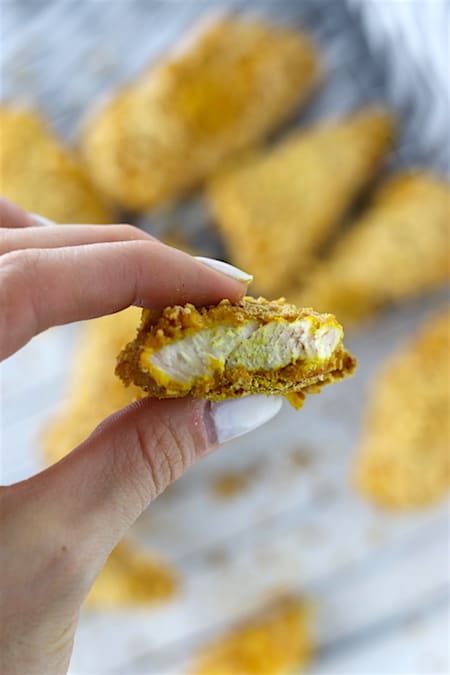 Holding a baked turmeric chicken tender