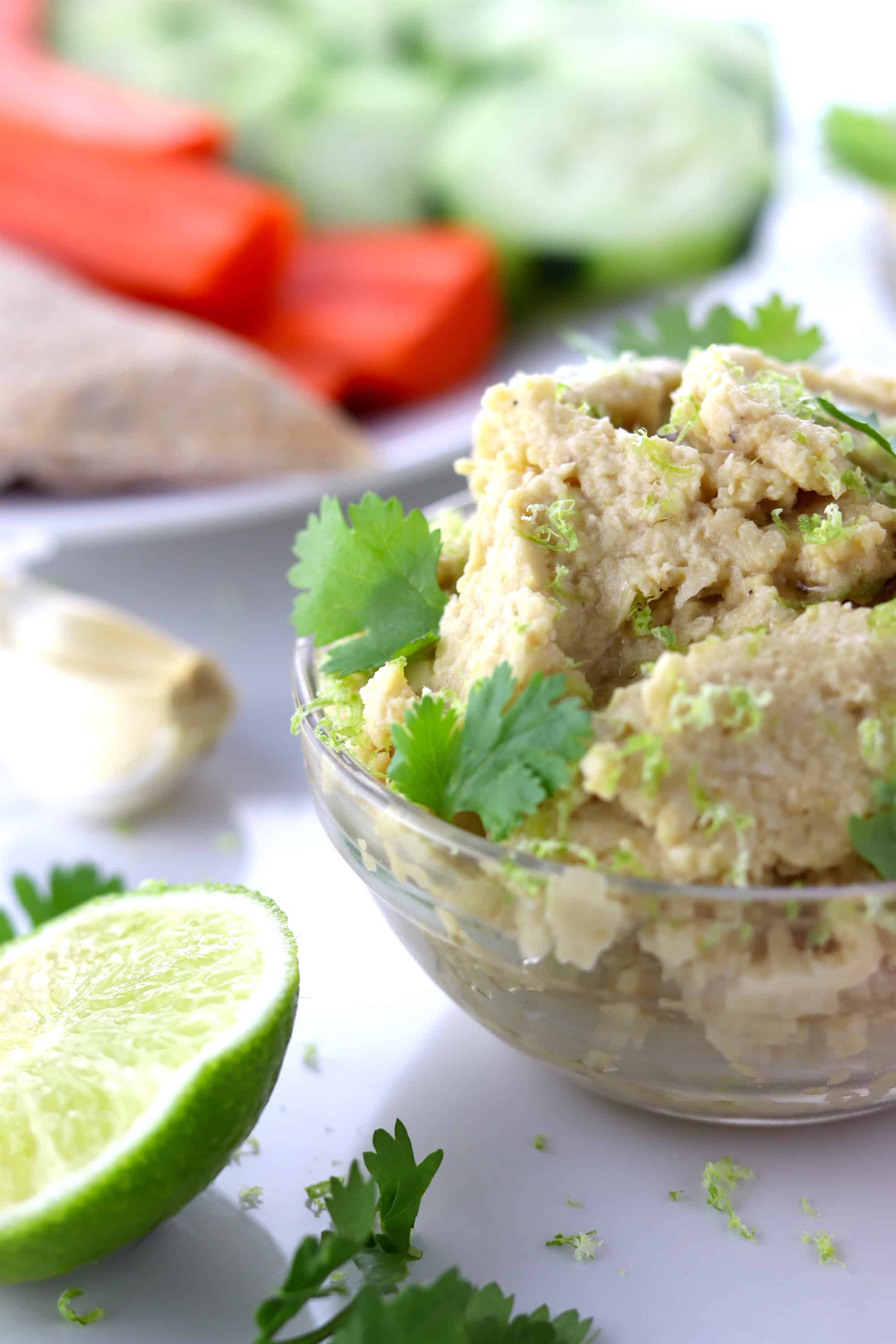 Simple roasted garlic and lime hummus in a dish with veggies and pita