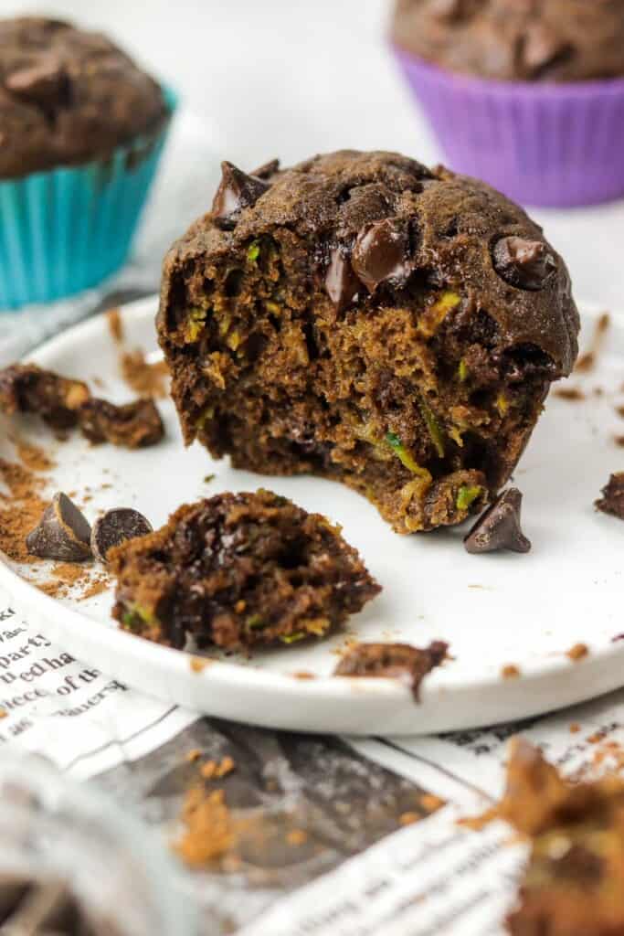 A half eaten chocolate zucchini muffin on a white plate.
