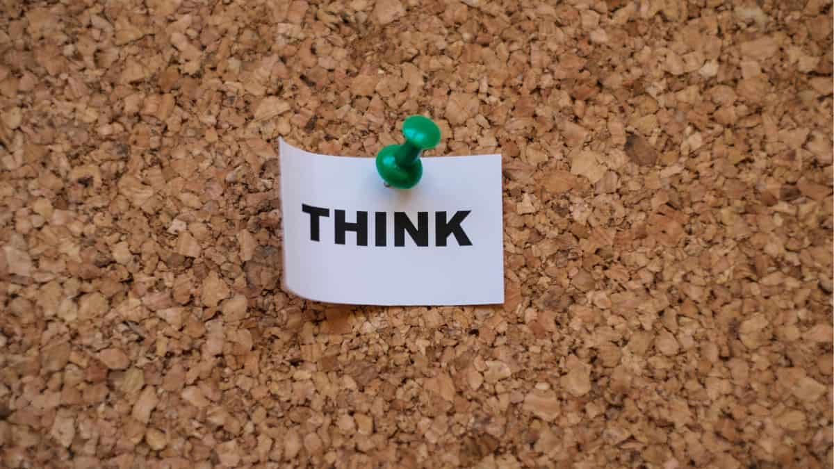 the word think on a slip of white paper held with a green thumbtack on cork board.