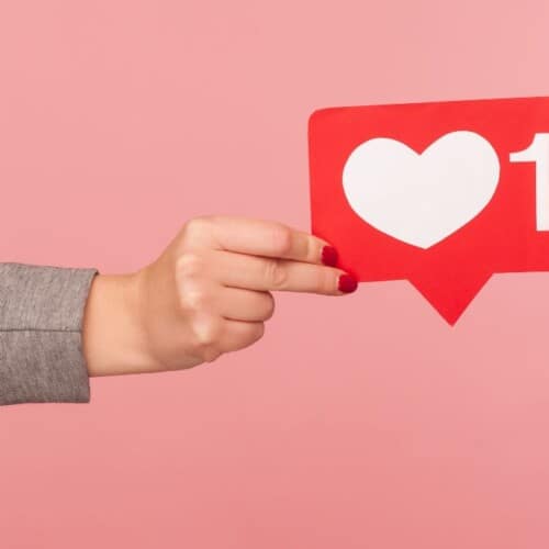 woman's hand holding a social media heart symbol.