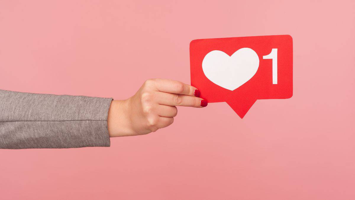 woman's hand holding a social media heart symbol.