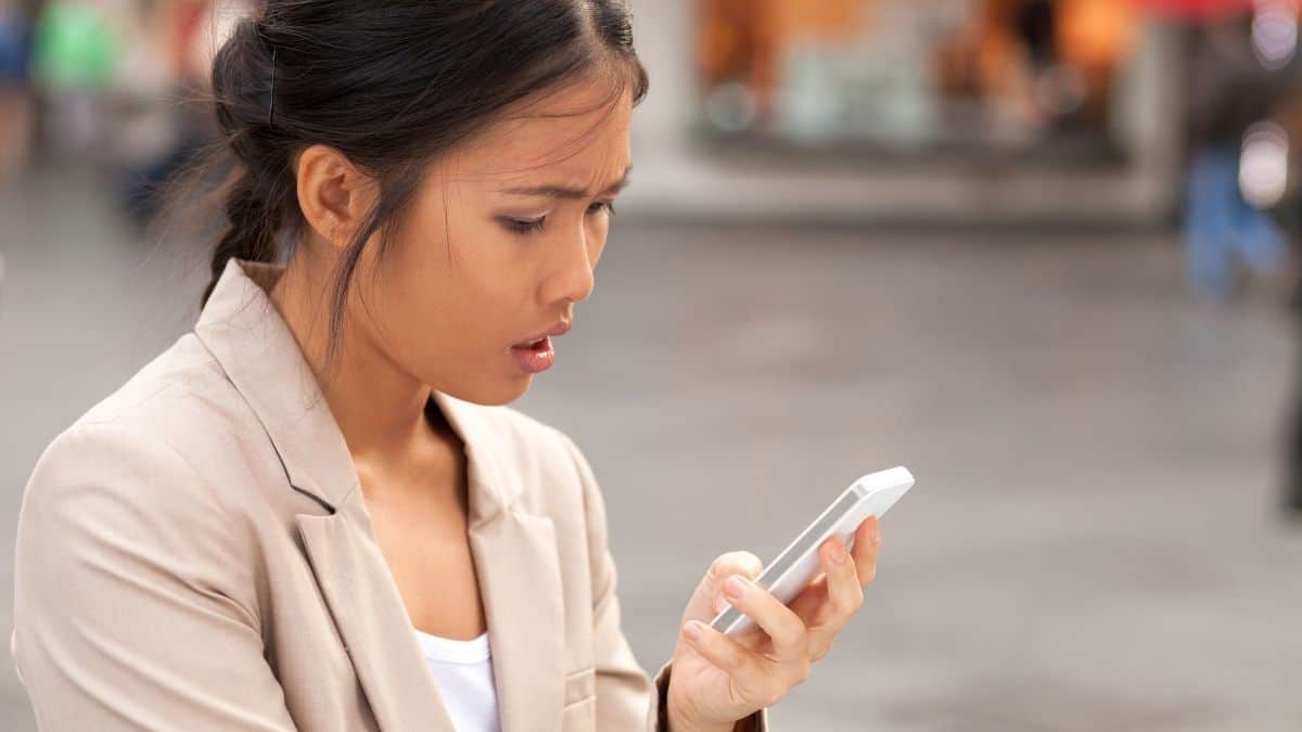 A woman in a tan blazer looking shocked at her phone