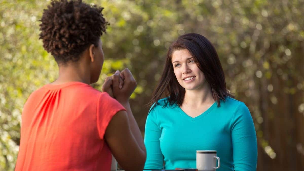 two women talking with eachother outside over coffee.