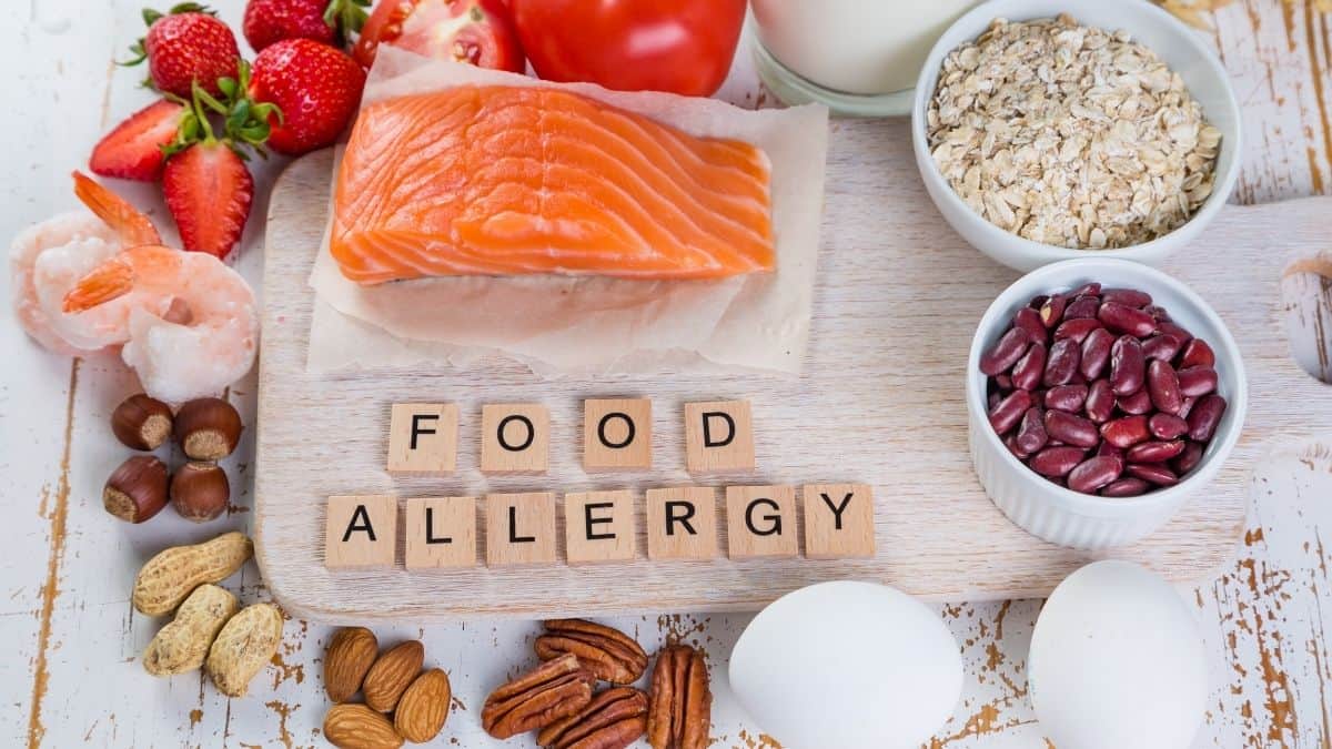 food allergy spelled out in scrabble tiles with raw fish, nuts and beans.