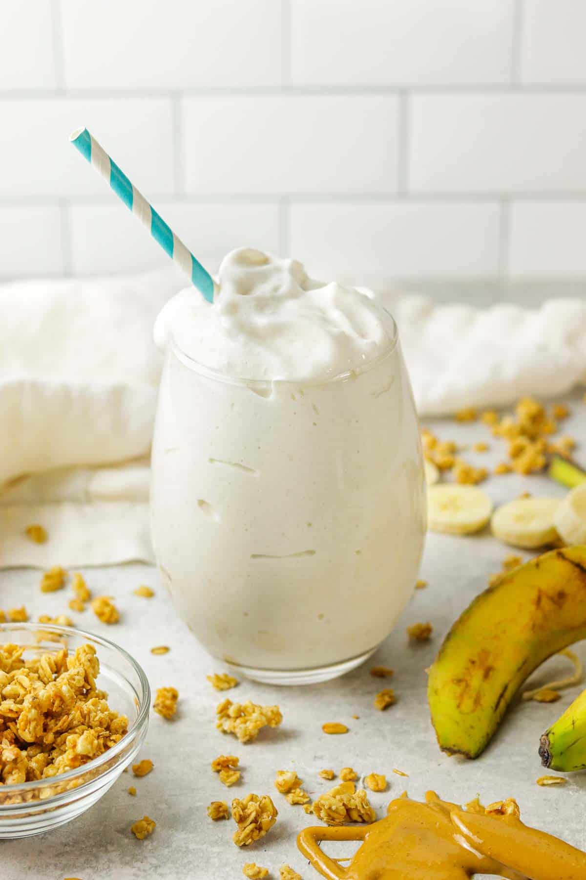 A banana protein shake on the counter with granola around it