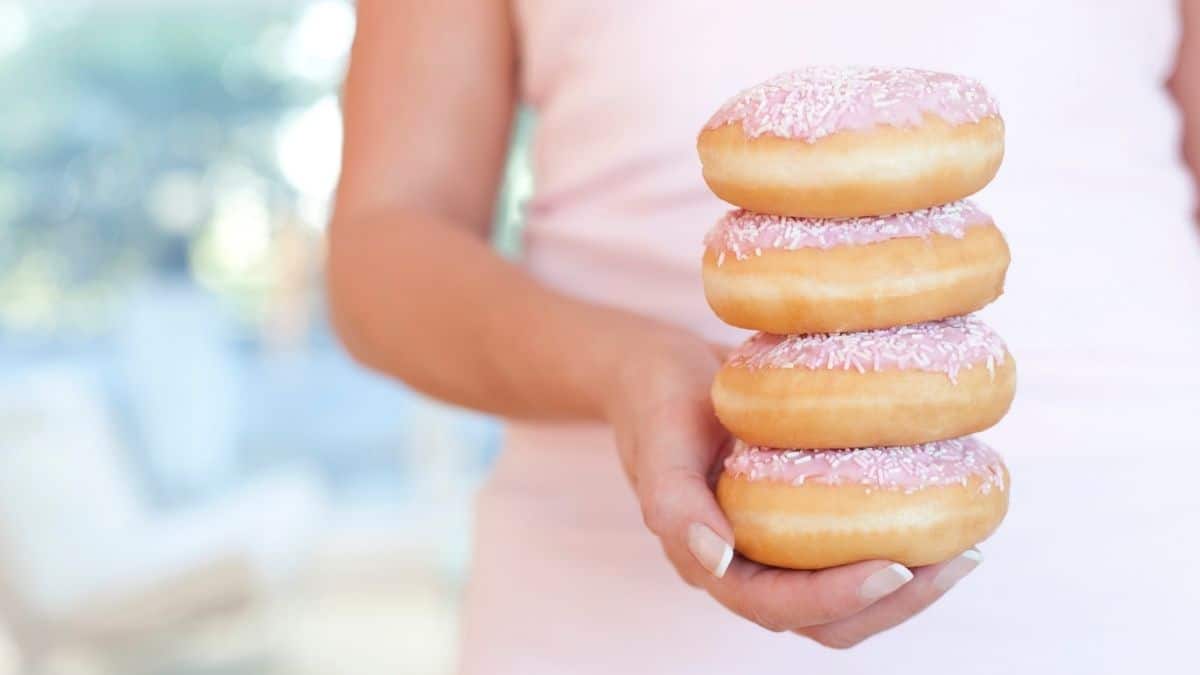 A woman holding a stack of pink frosted donuts.