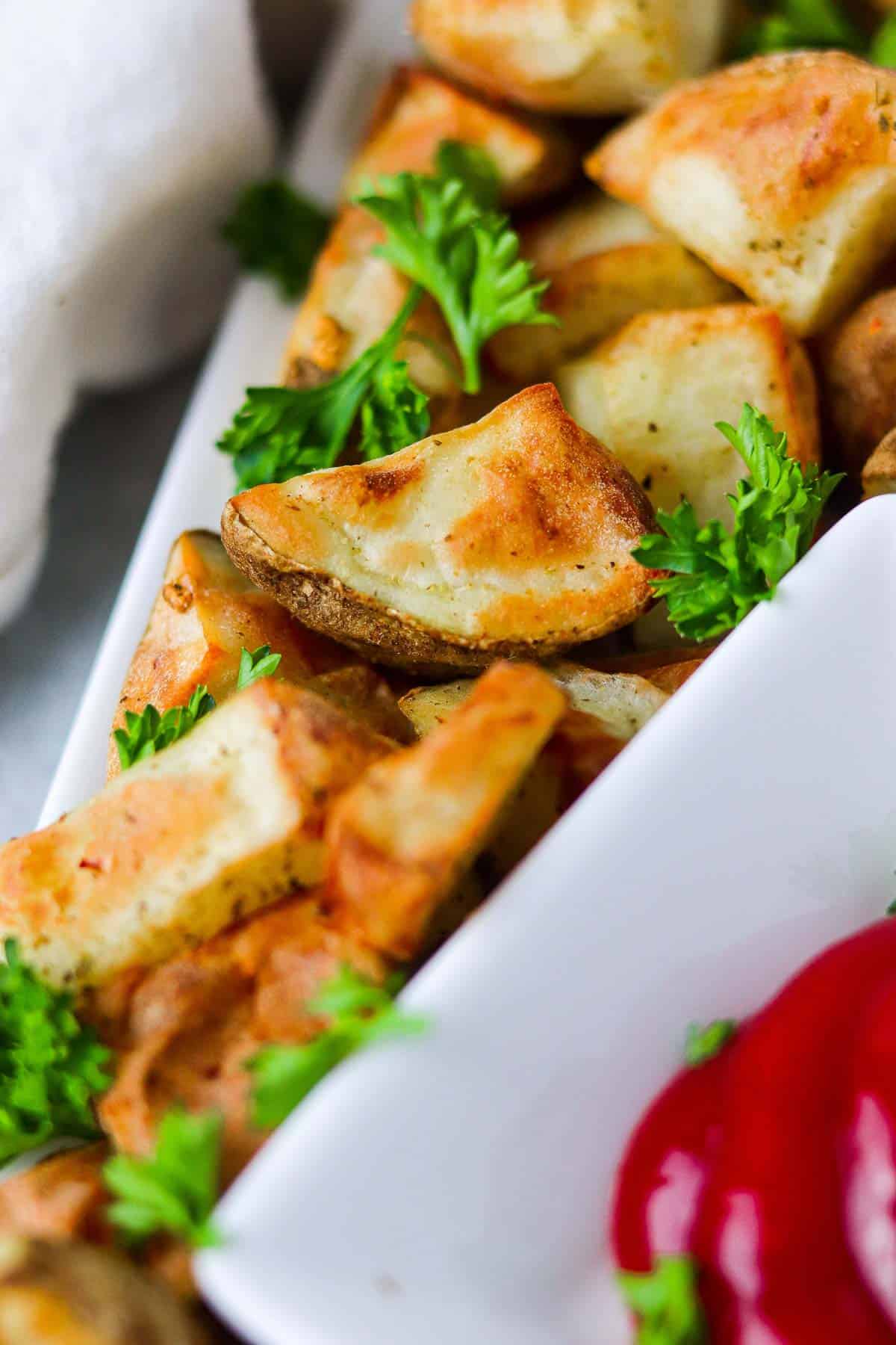 Up close potato cubes, garnished with parsley and a side of ketchup.