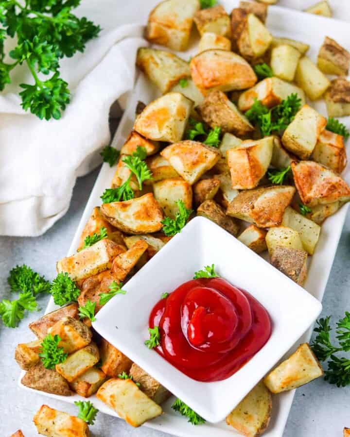 Potato cubes on a white plate, garnished with parsley and with a side of ketchup.