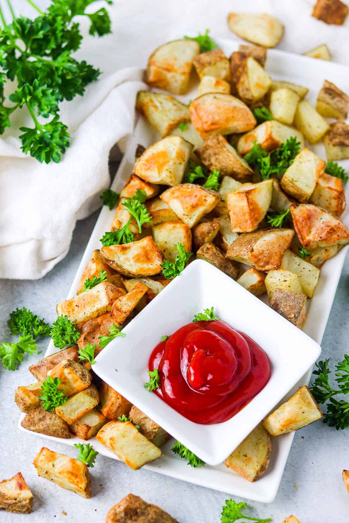 Potato cubes on a white plate, garnished with parsley and with a side of ketchup.