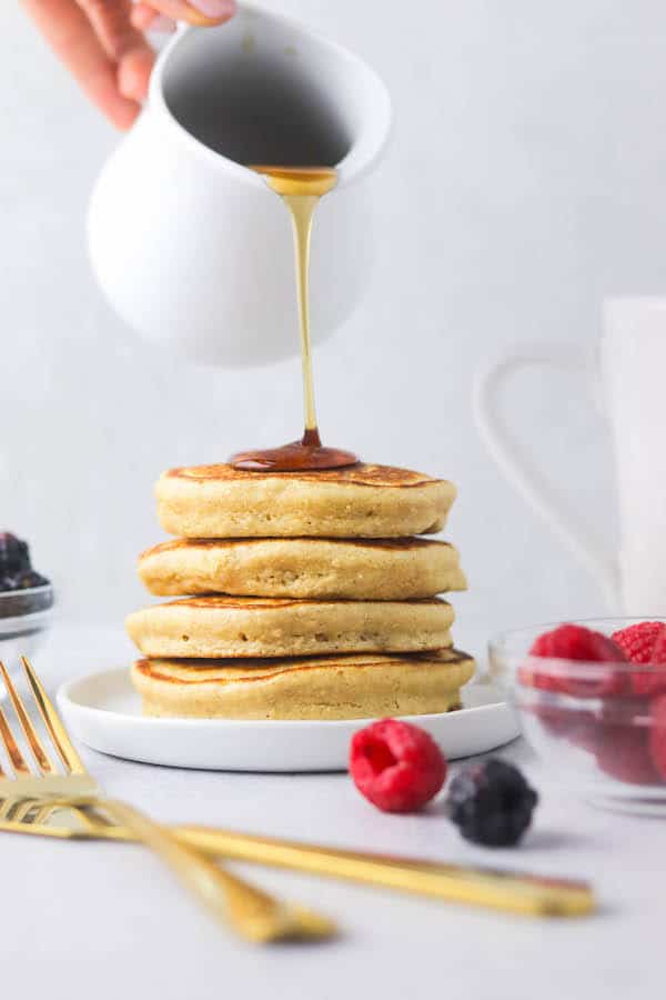 A stack of pancakes with maple syrup being poured on top.