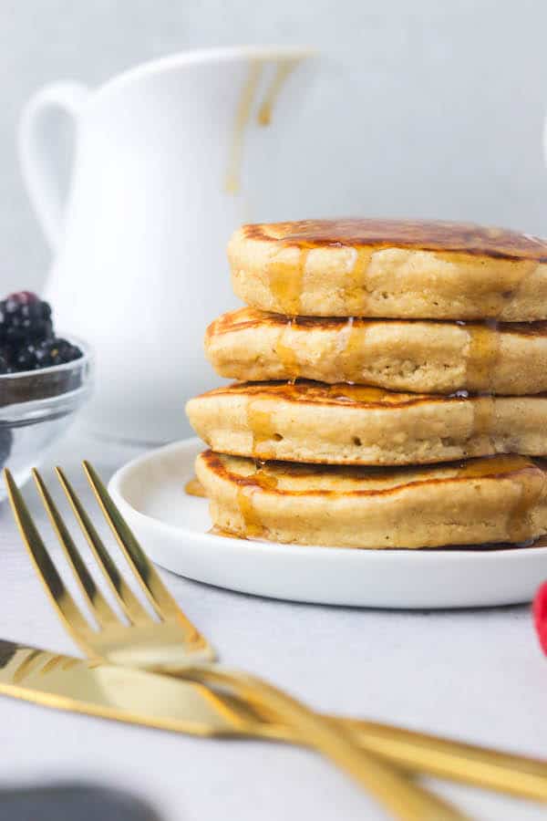 a close up of a stack of pancakes, with a knife and fork in the foreground