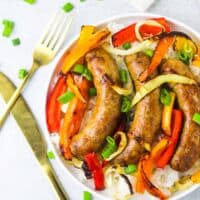 A plate of sausage and peppers on a white background with gold silverware.