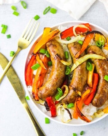 A plate of sausage and peppers on a white background with gold silverware.