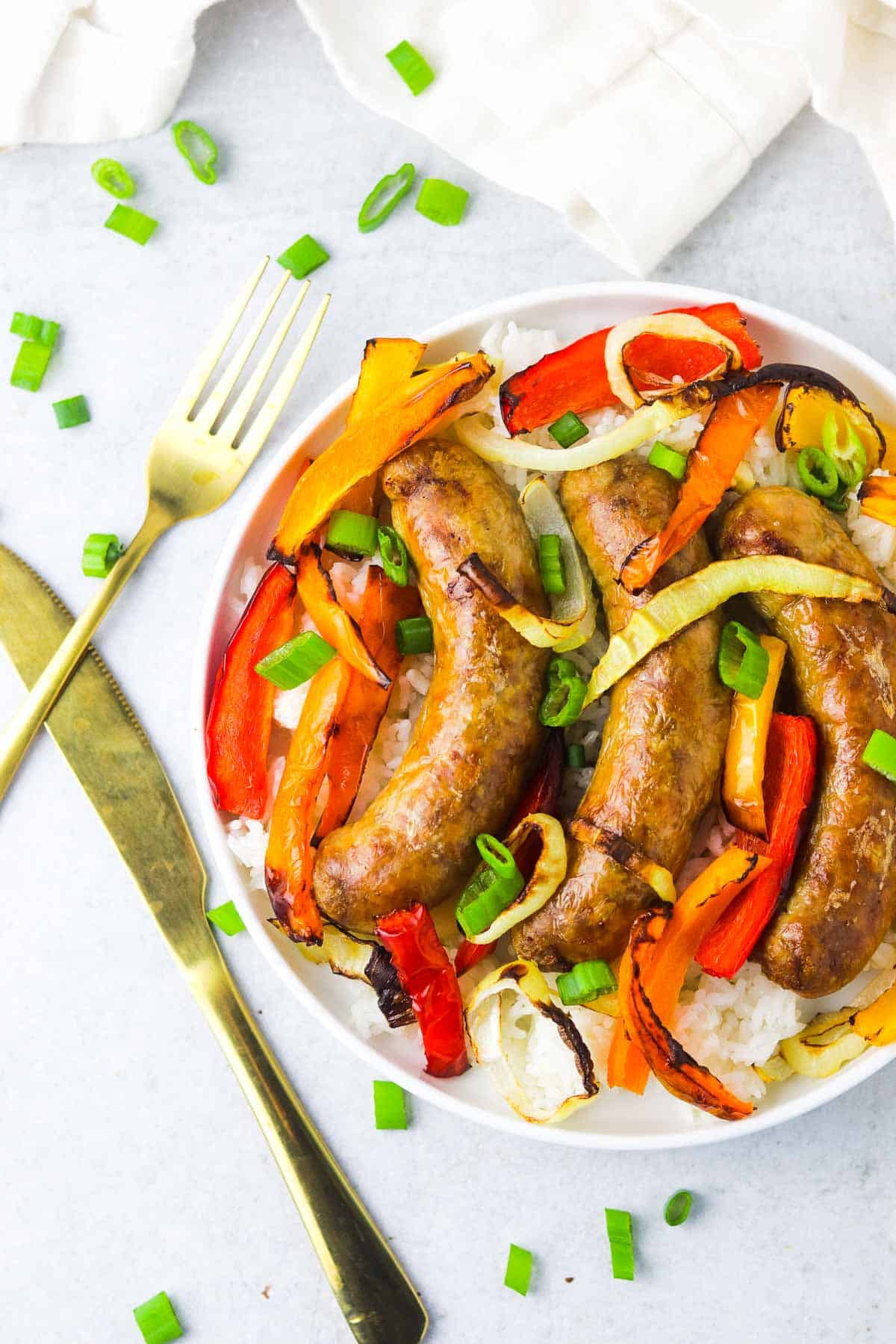 A plate of sausage and peppers on a white background with gold silverware.