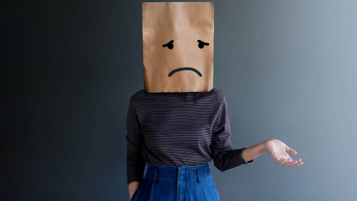 woman with paper bag on her head with a sad face drawn on.