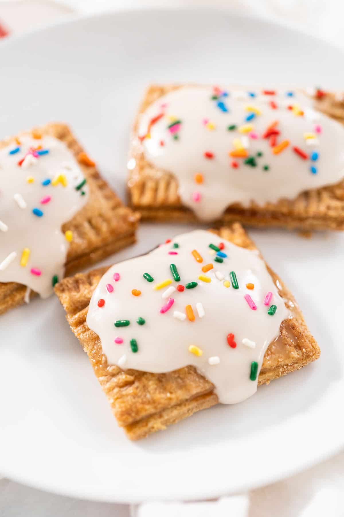 3 vegan pop tarts with icing and sprinkles on a white plate.