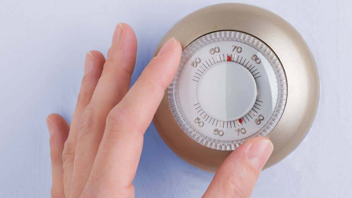 A hand changing the temperature on a thermostat