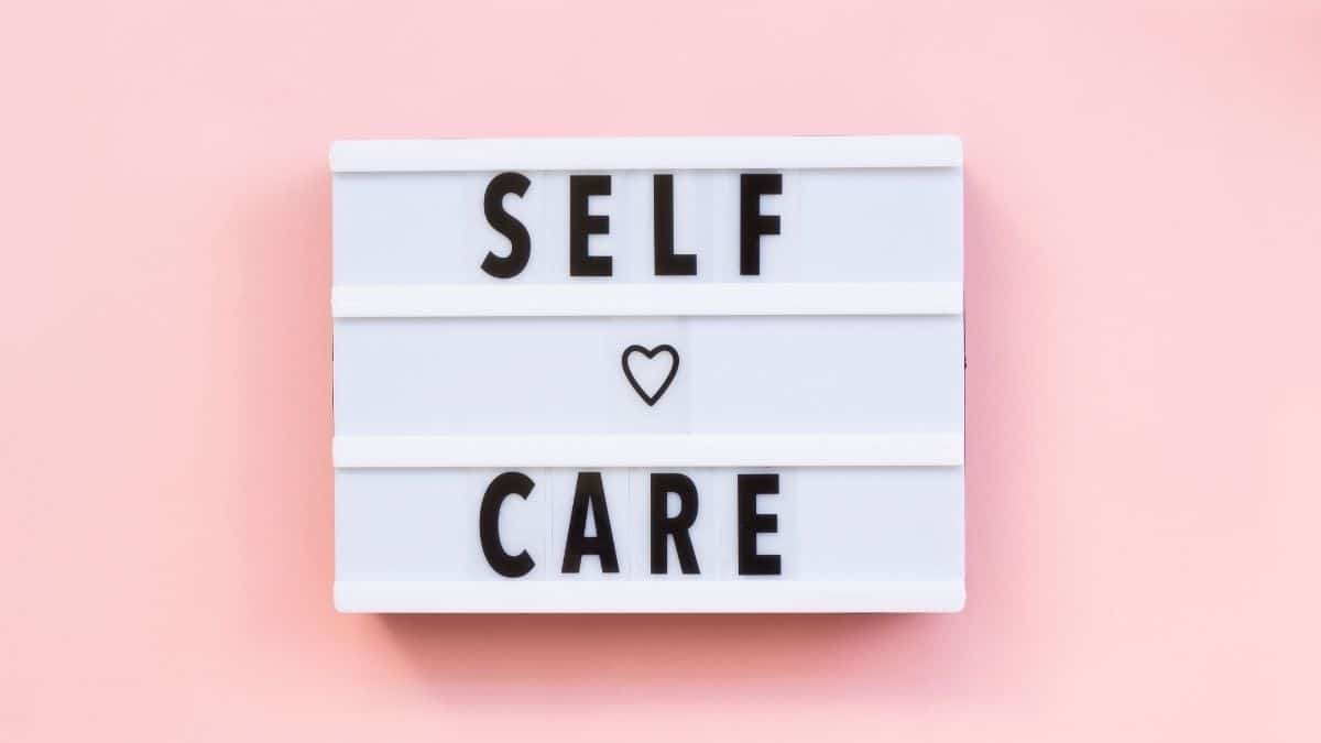 White sign with the words self care spelled out on a pick background