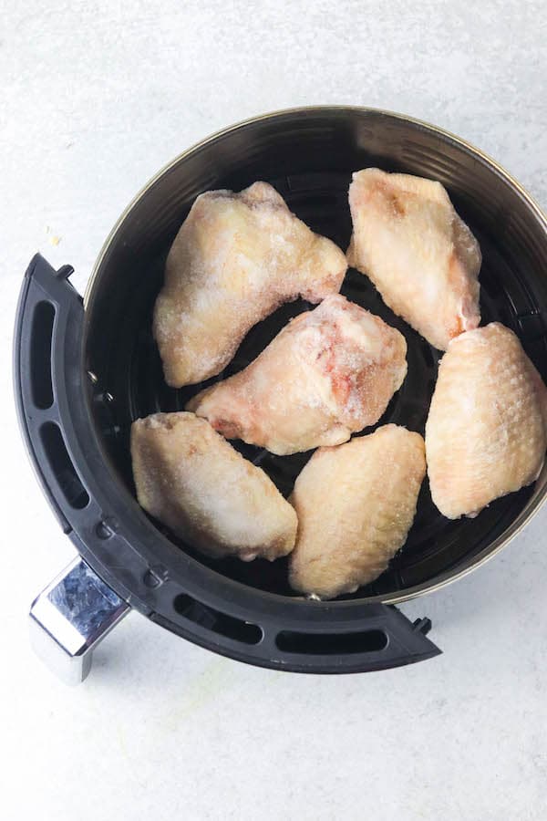 The basket of an air fryer with frozen chicken wings inside.