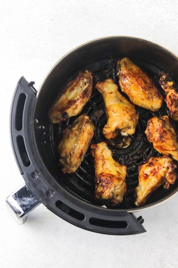 The basket of an air fryer with cooked frozen chicken wings
