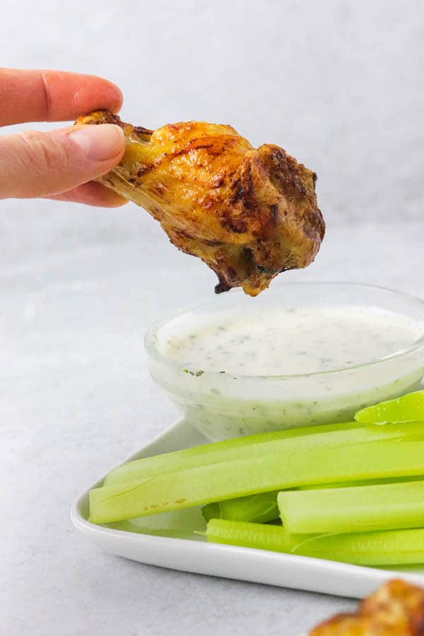 A cooked chicken wing, being dipped into a creamy sauce.