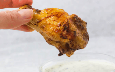 A chicken wing being dipped into a creamy sauce.