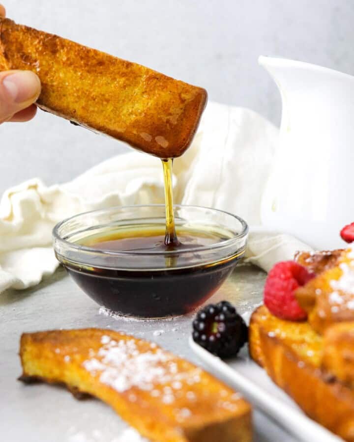 Dipping an air fryer french toast stick int maple syrup.