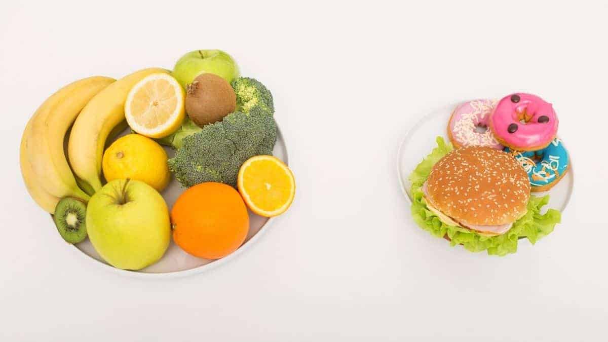 A bowl of fruit on a plate and a donut with a burger on another plate.