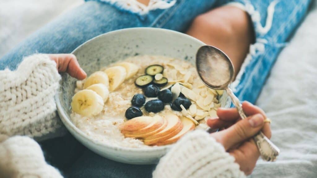 A person holding a bowl of oatmeal topped with fruit.
