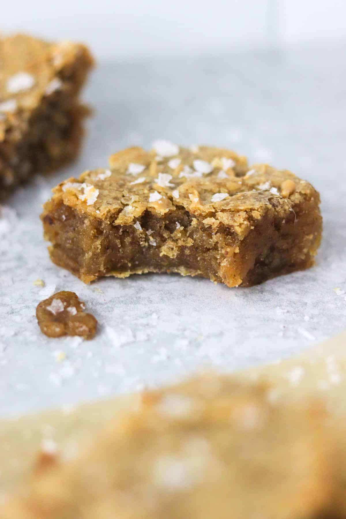 A close up of a gooey peanut butter vegan blondie with a bite out.