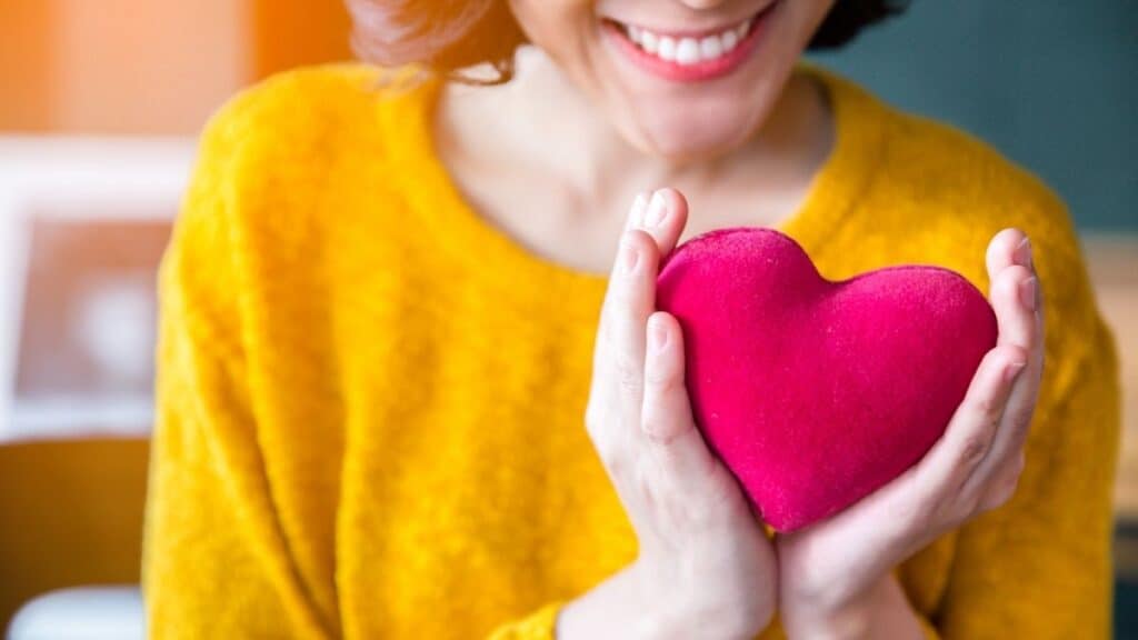 A woman smiling at the camera holding a pink plush heart.