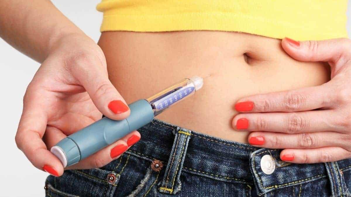 A woman in a yellow tank top and jeans taking insulin.