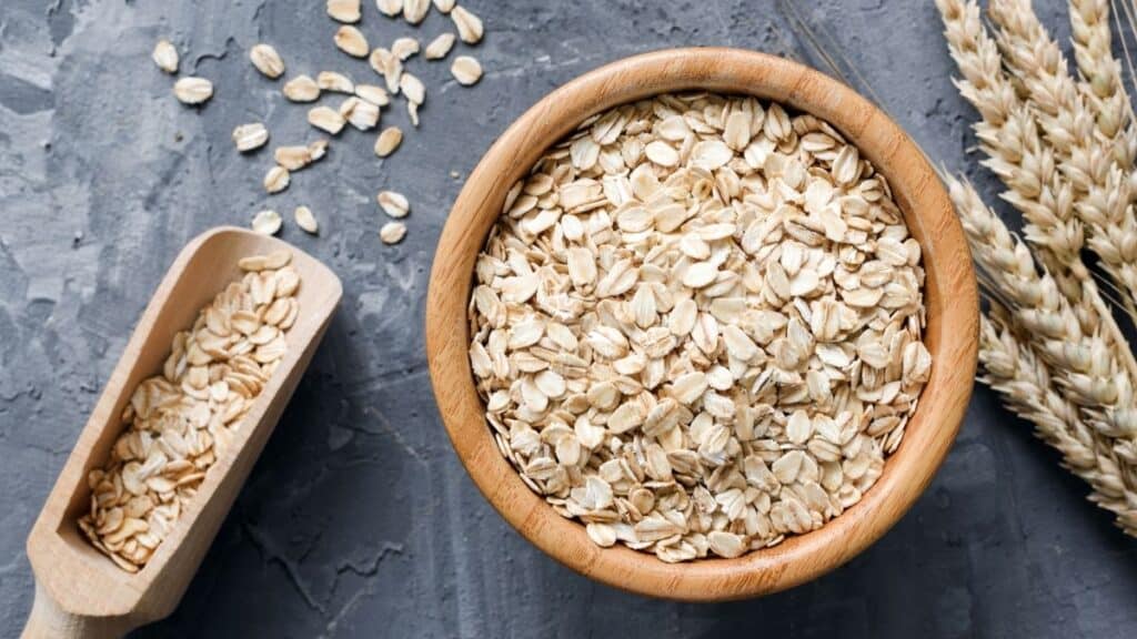 A wooden bowl of oats with a scoop on a dark slate background.