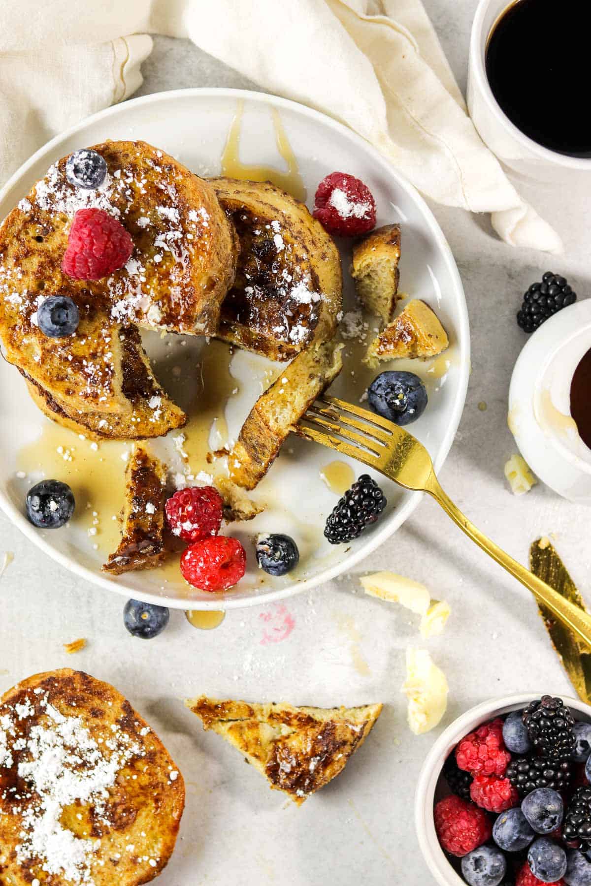 plate of sourdough french toast with berries, maple syrup and powdered sugar.