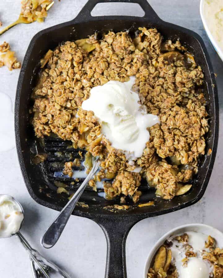 A skillet full of old fashioned apple crisp topped with ice cream.