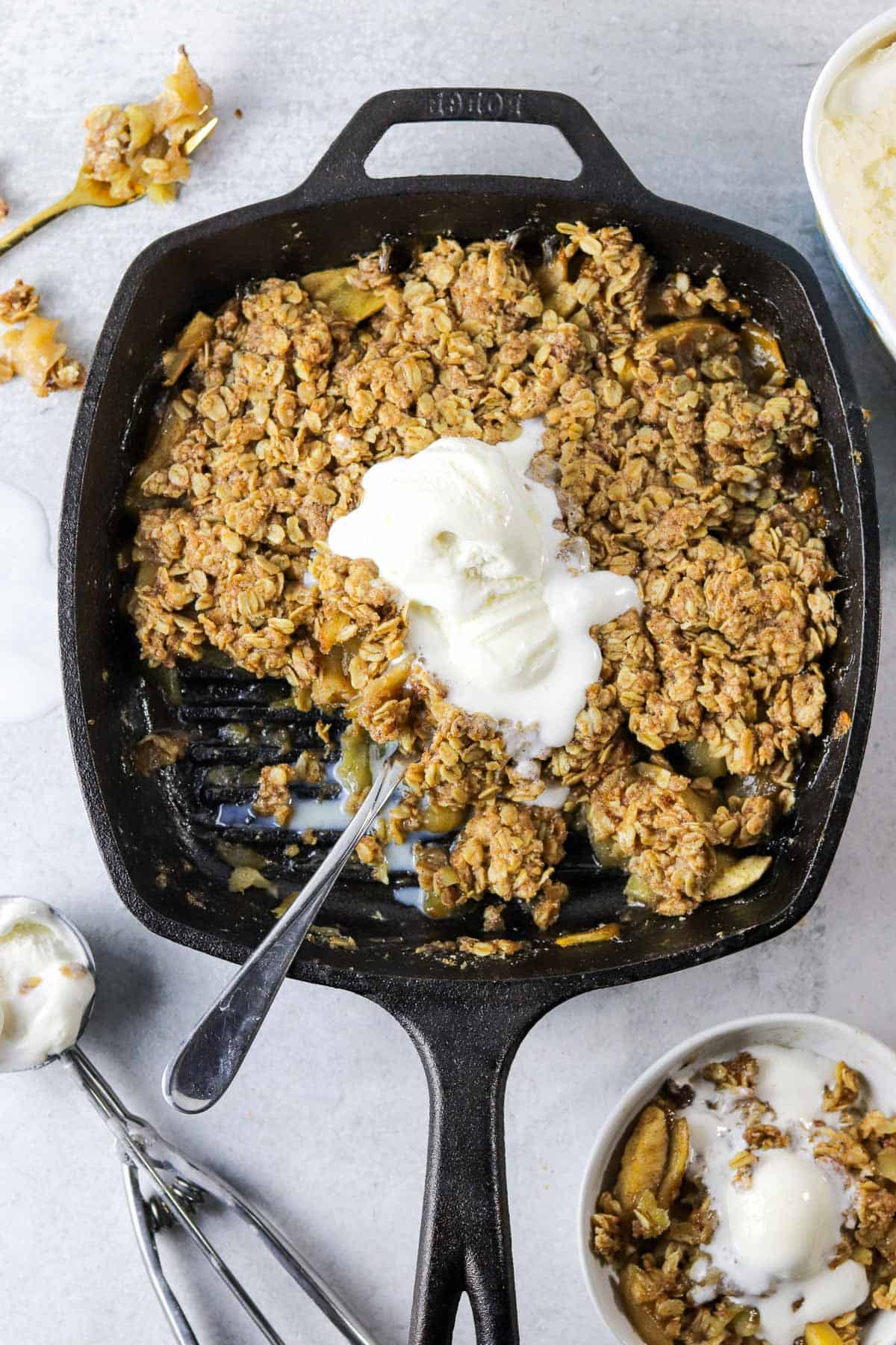 A skillet full of old fashioned apple crisp topped with ice cream.