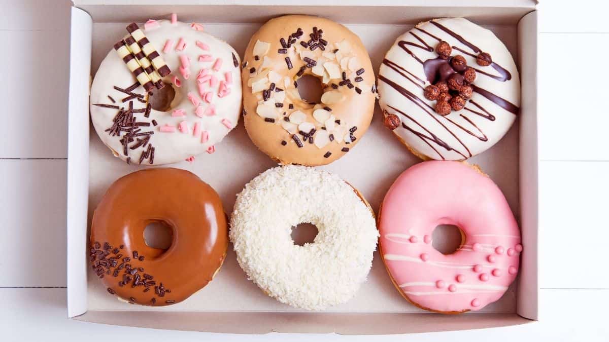 A box filled with different kinds of pink and brown decorated donuts.