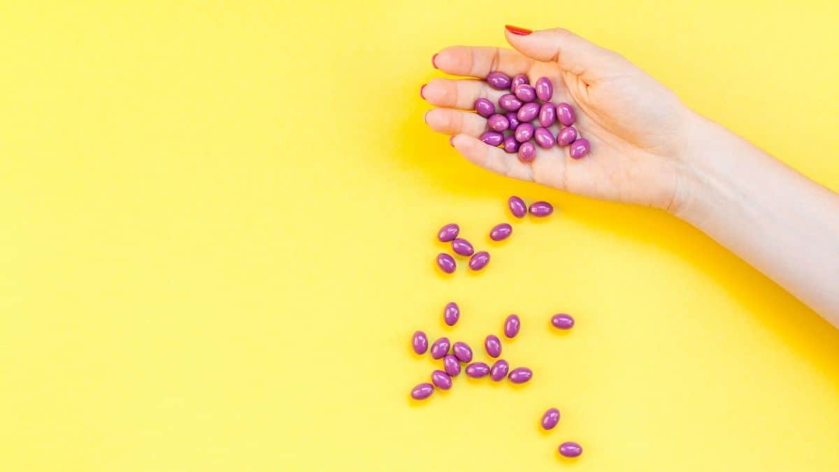 A hand dropping a handful of purple supplements in front of a yellow background.