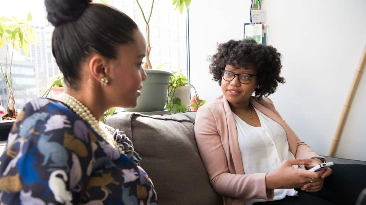 Two women talking to each other on a couch.