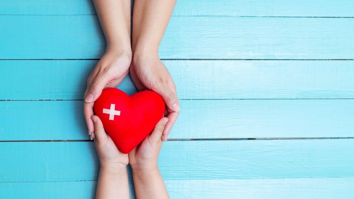 two hands holding a red heart with a white cross on it over a blue background.