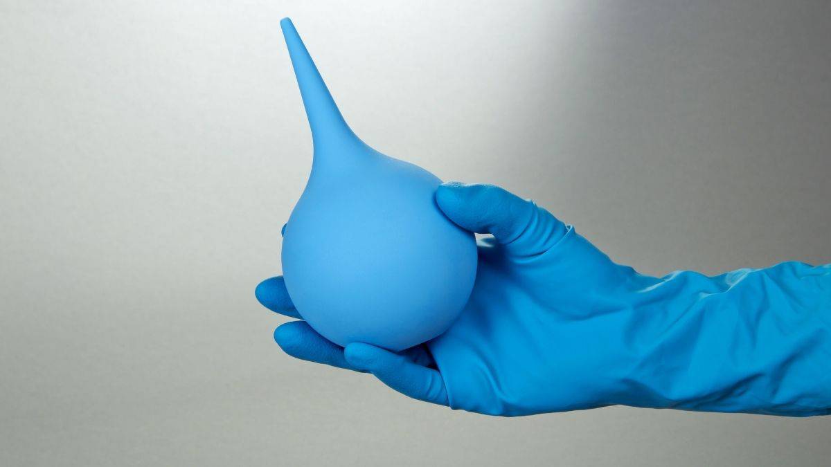 Colonic and enema blue tubes held by a blue gloved hand.