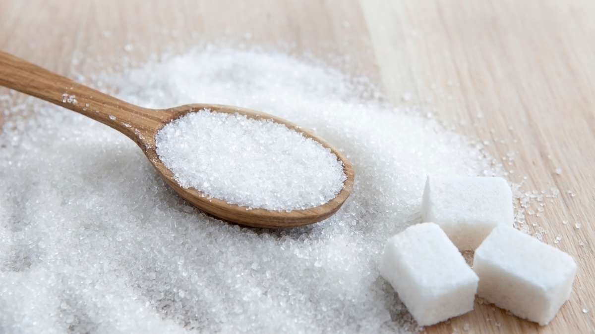 Sugar cubes and a spoonful of sugar on a wood surface.