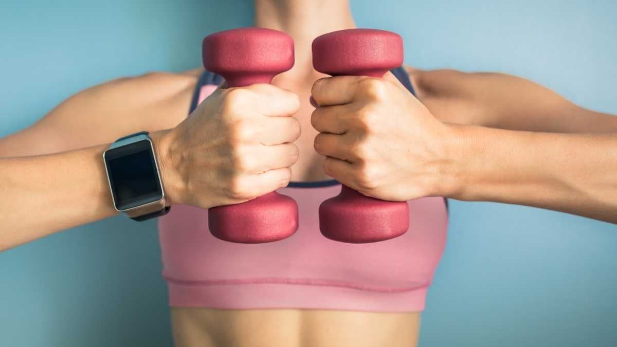 Woman in a pink sports bra holding pink dumbbells.