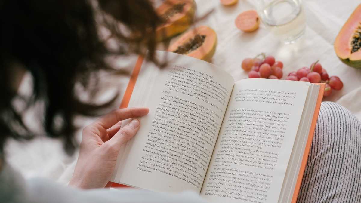 Woman reading a book with fruit in the background.