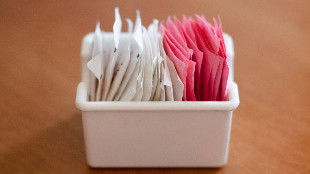 Sugar and artificial sugar packets in a white box on a table.