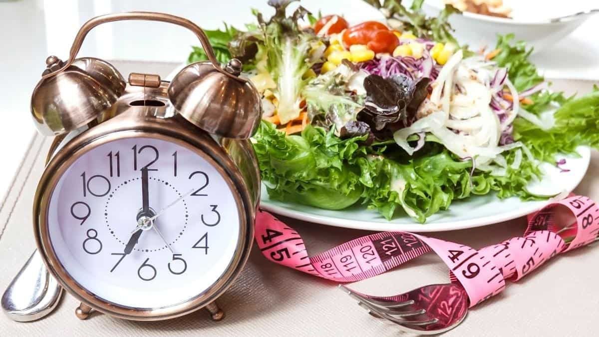 a salad on a plate with a tape measure and an alarm clock..