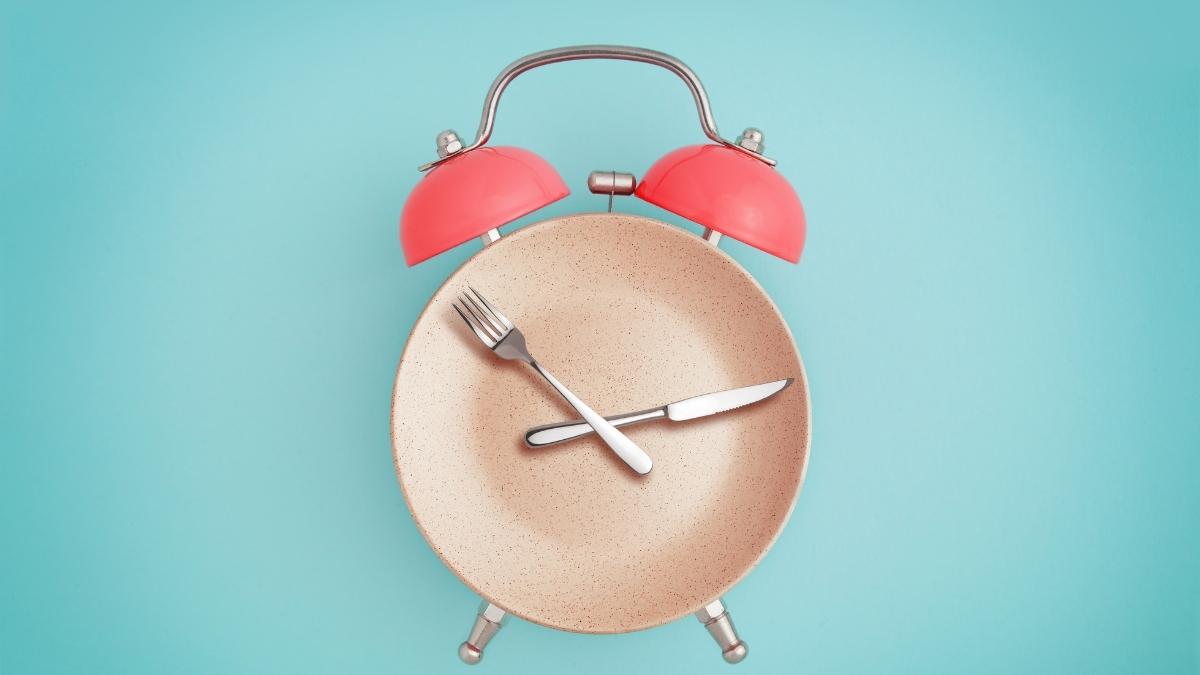 plate, fork and knife laid out like a clock on a blue background.