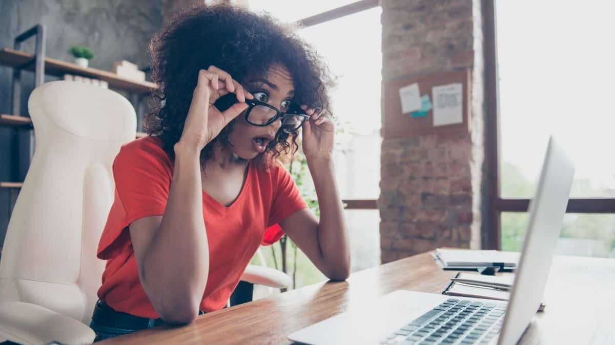 A woman in a red top looking shocked at her computer.