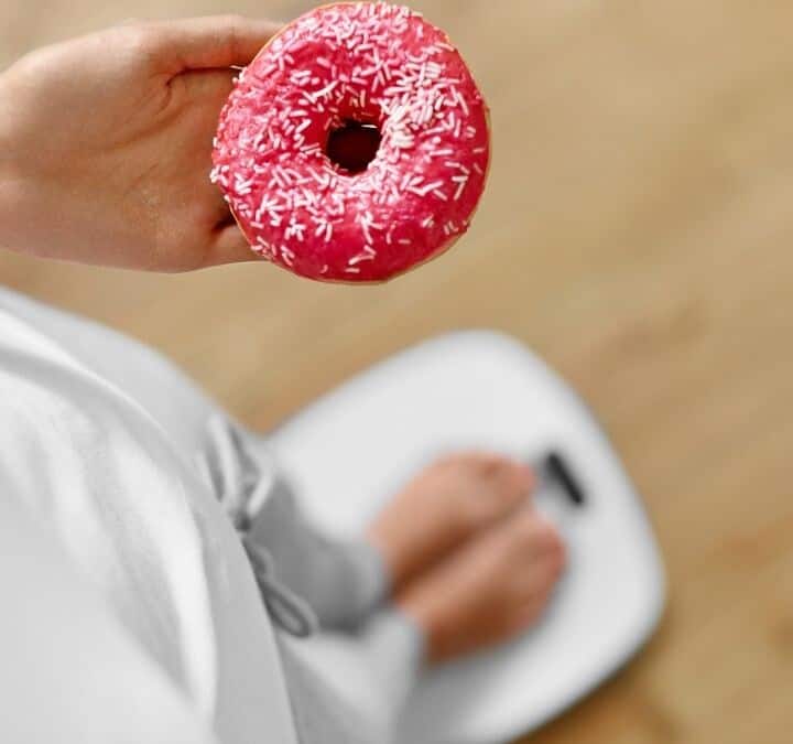 a woman holding a donut while standing on a scale.